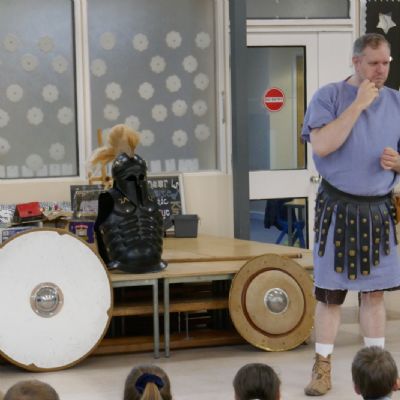 Ancient Greek presenter and  the pupils are in the foreground.