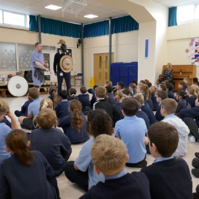 Ancient Greek presenter and our teacher in a helmet with a shield  and the pupils are in the foreground.