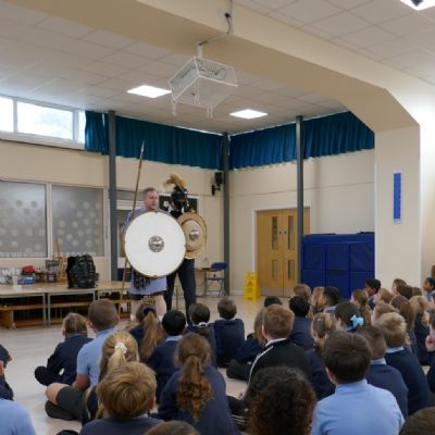 Ancient Greek presenter and our teacher in a helmet with a shield and spear with pupils in the foreground.