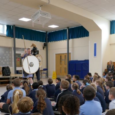 Ancient Greek presenter and our teacher in a helmet with a shield and spear with pupils in the foreground.